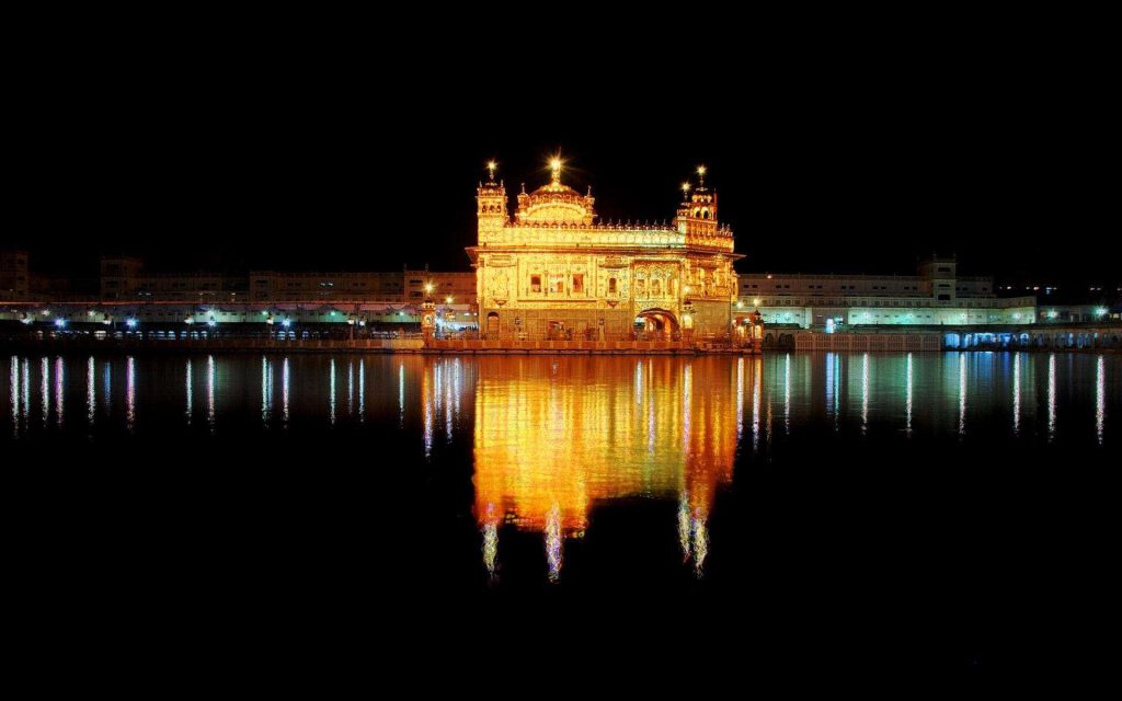 Golden Temple illuminated at night in Amritsar with glowing reflections on calm sarovar waters Wallpaper