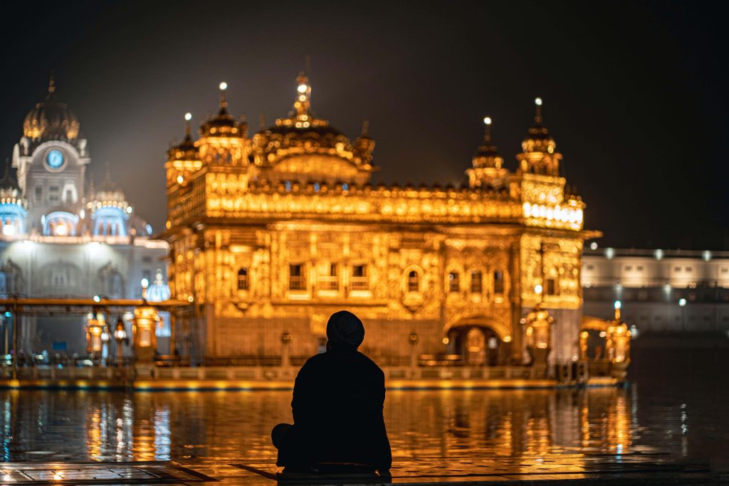 Man in turban reflecting silently before illuminated Golden Temple at night serene wallpaper
