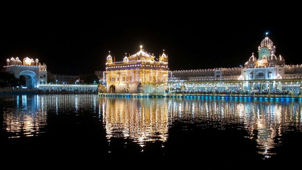 Golden Temple at night glowing with reflection on calm Amrit Sarovar in Amritsar serene view Wallpaper