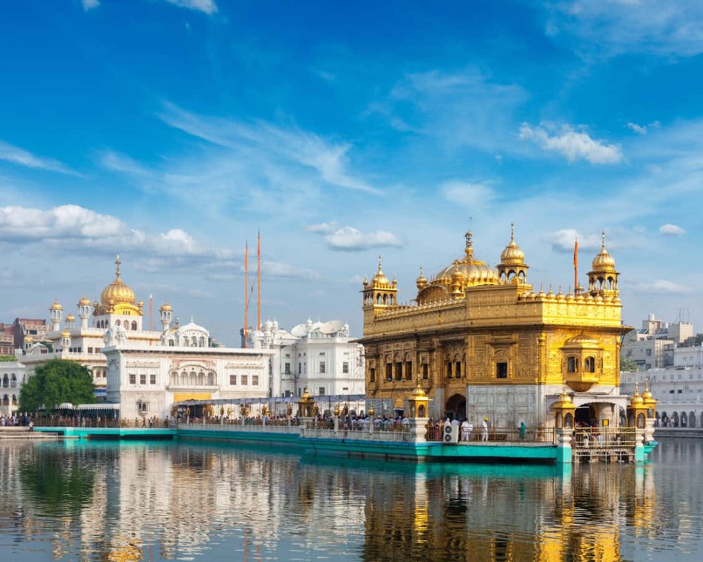 Golden Temple Harmandir Sahib reflected in water with green causeway under blue sky wallpaper