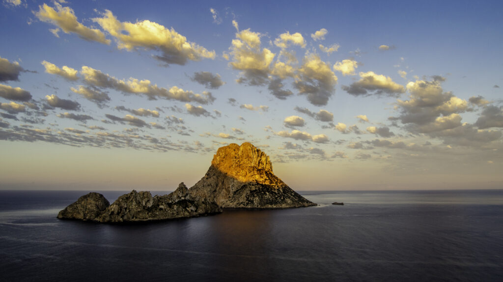 Dramatic twilight seascape with golden-lit rugged rock formation calm deep blue waters wallpaper