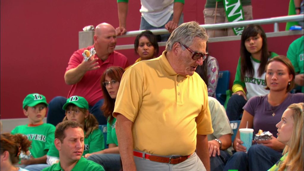 Good Luck Charlie football game scene with man in yellow polo and Denver fans in green jerseys Wallpaper