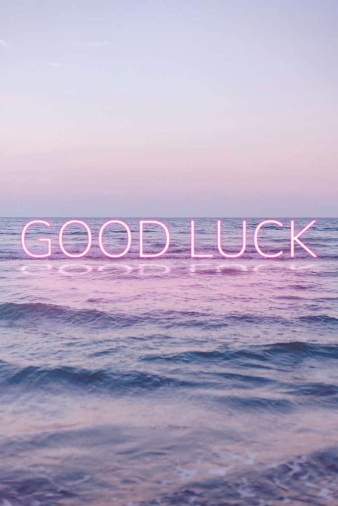 Glowing pink GOOD LUCK neon sign over pastel ocean twilight waves minimalist wallpaper background