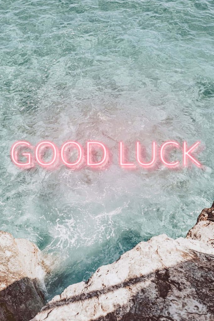 Good Luck neon sign glowing pink above turquoise ocean and rugged rocks wallpaper background