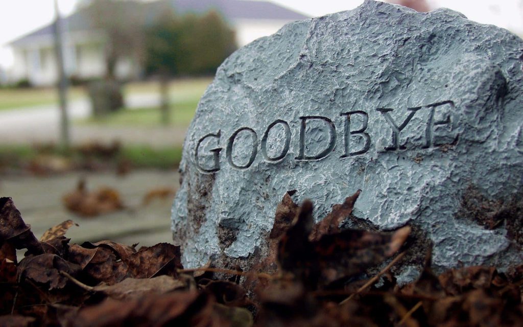Close-up of engraved grey stone with goodbye among autumn leaves moody reflective wallpaper background