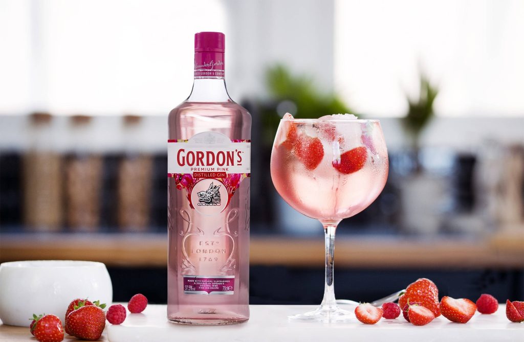Gordons Premium Pink Gin bottle with strawberry raspberry cocktail in bright summer setting Wallpaper