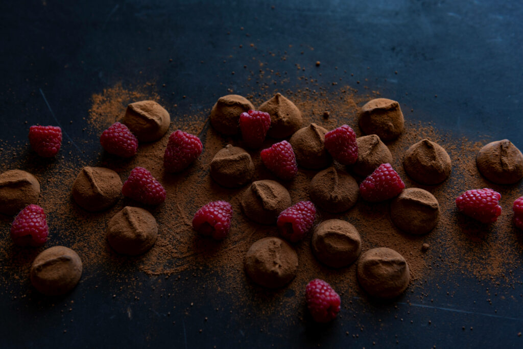 Chocolate bites dusted with cocoa powder paired with fresh raspberries on dark background Wallpaper