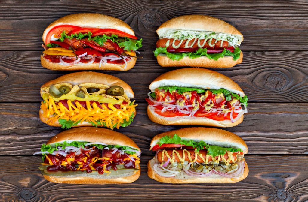 Six gourmet hot dogs with fresh toppings on rustic dark wooden table high quality food photo Wallpaper