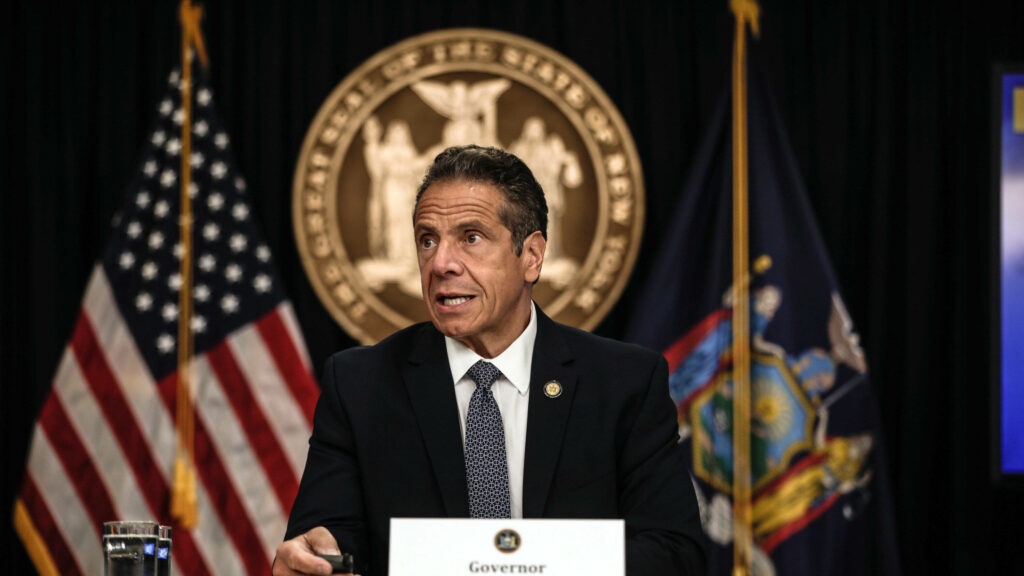 Governor Andrew Cuomo speaking at press conference with American flag and New York State seal background Wallpaper