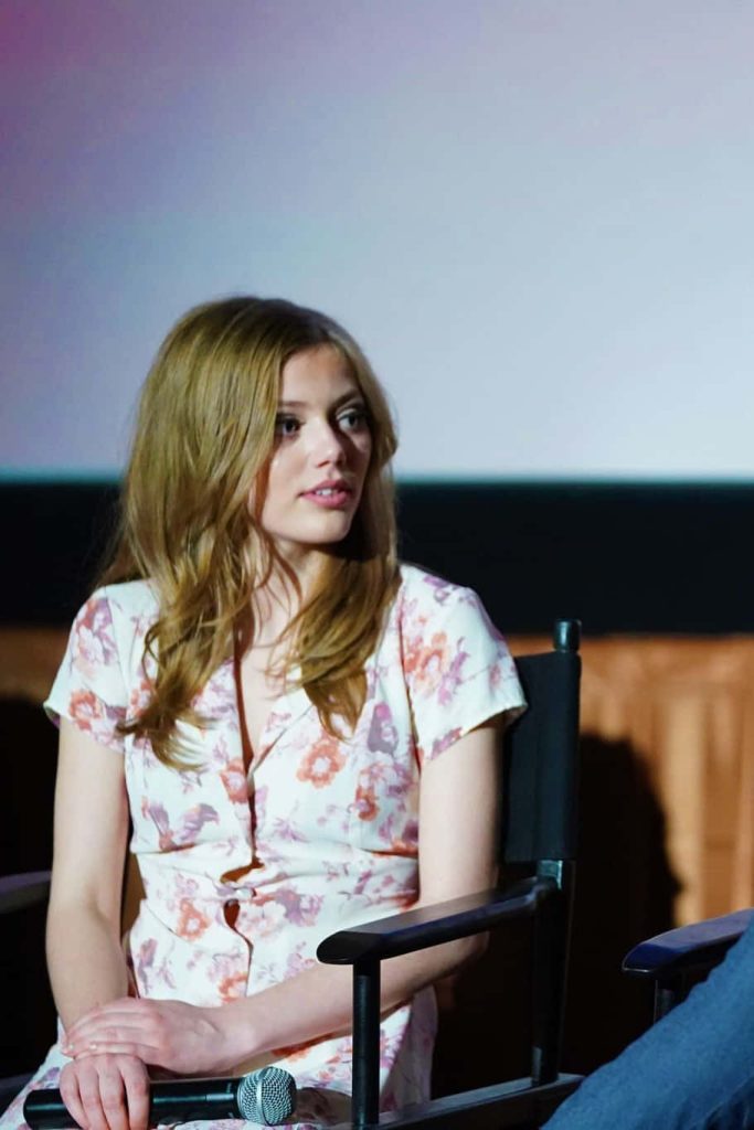 Grace Van Dien at panel discussion in floral blouse holding microphone sitting on director chair Wallpaper