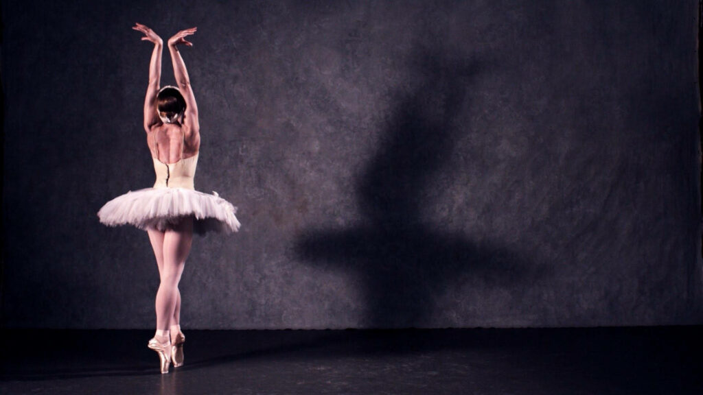 Ballet dancer in white tutu en pointe stretching arms gracefully in softly lit studio background Wallpaper