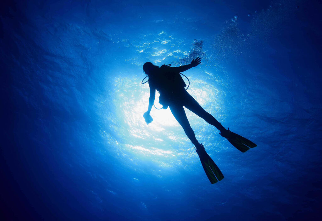 Lone diver descending through clear blue waters with sunlight rays illuminating serene underwater scene Wallpaper