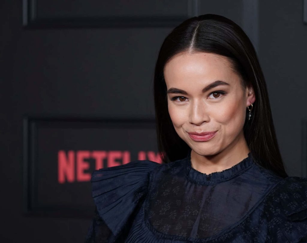 Genevieve Kang in navy ruffled blouse at Netflix event red carpet with blurred logo background Wallpaper
