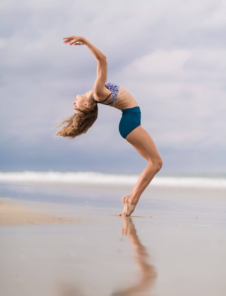Flexible woman in graceful gymnastics backbend on sandy beach with ocean reflection background Wallpaper