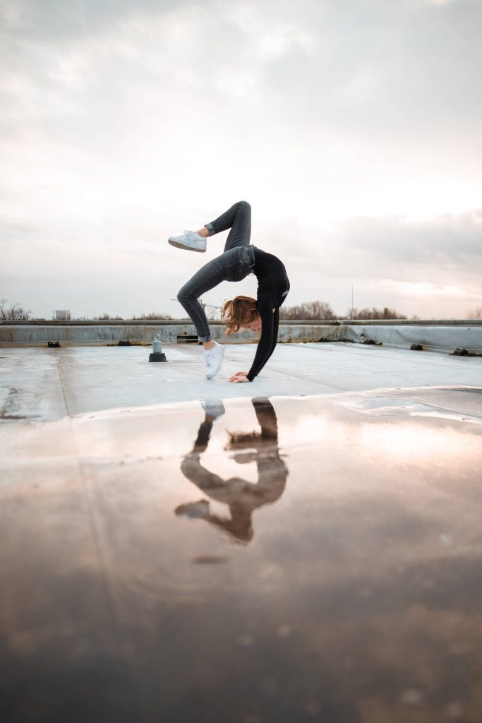 Flexible gymnast performing scorpion backbend on wet rooftop with moody urban reflection wallpaper