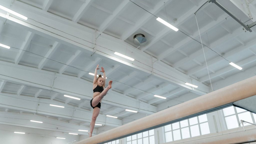 Young gymnast performing split on balance beam in bright gym showcasing strength and focus Wallpaper