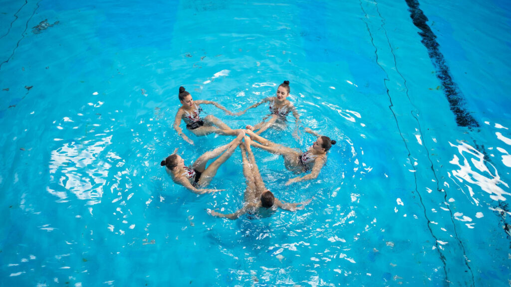 Synchronized swimmers in a bright blue pool forming a circular pattern showcasing teamwork Wallpaper