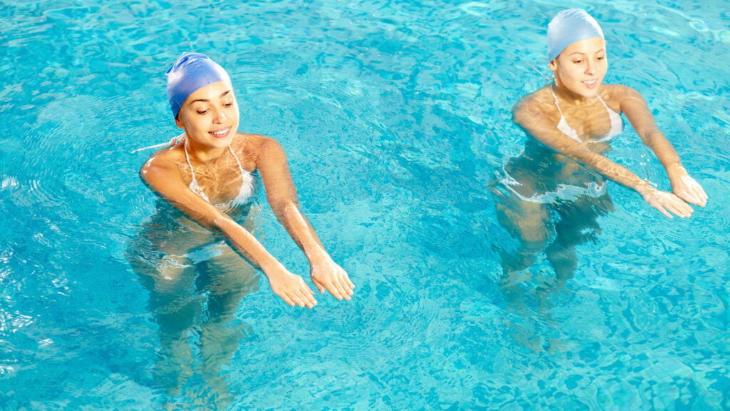 Two synchronized swimmers perform a graceful routine in clear blue water artistic swimming competition Wallpaper