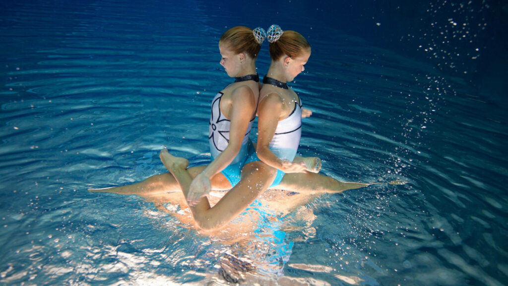 Two young girls performing synchronized swimming routine underwater showcasing teamwork and balance Wallpaper