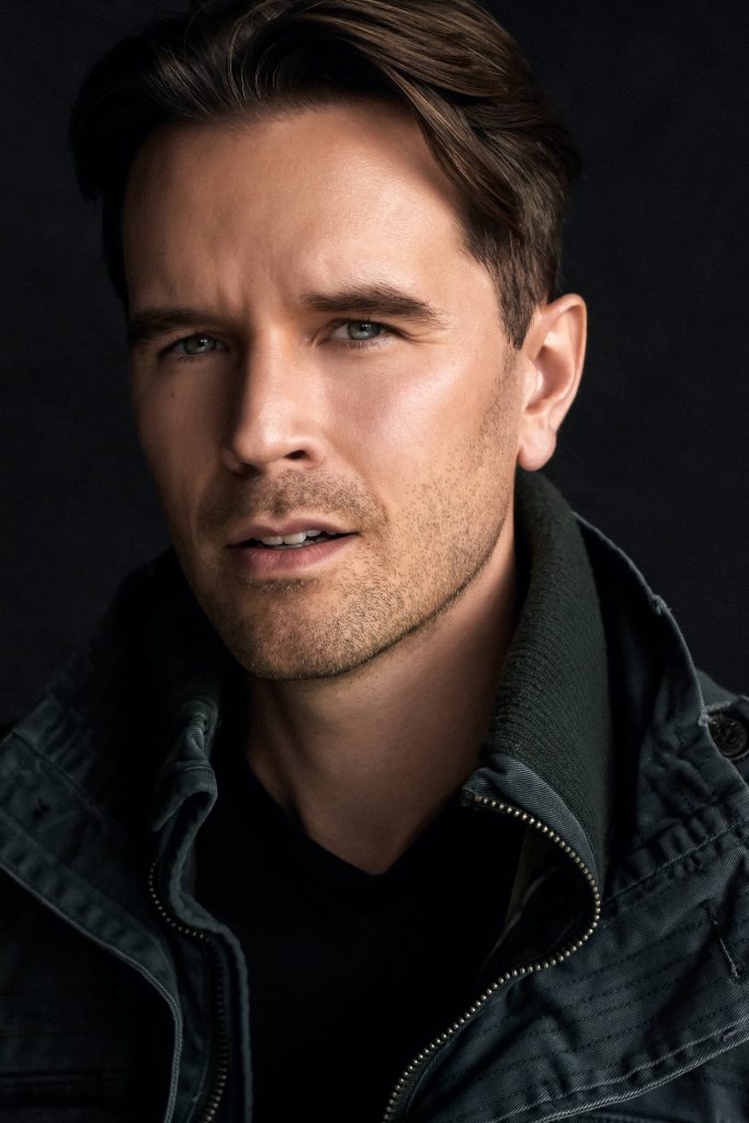 Cinematic close-up portrait of actor Graham Wardle in dark utility jacket on black background Wallpaper