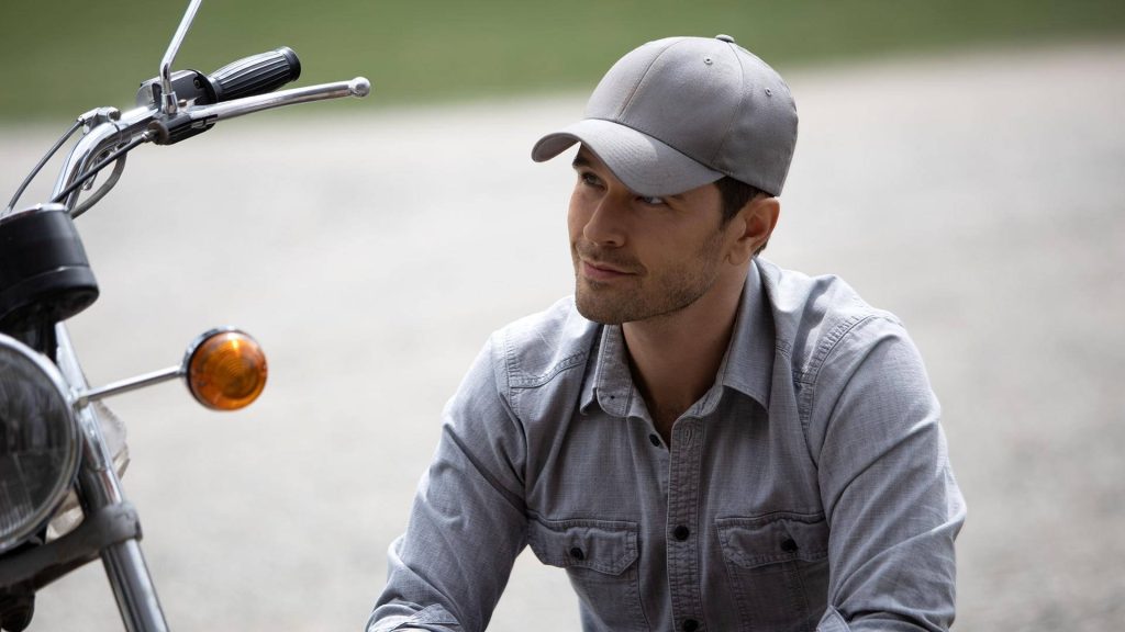 Graham Wardle in gray cap and shirt by motorcycle with soft natural light Heartland wallpaper