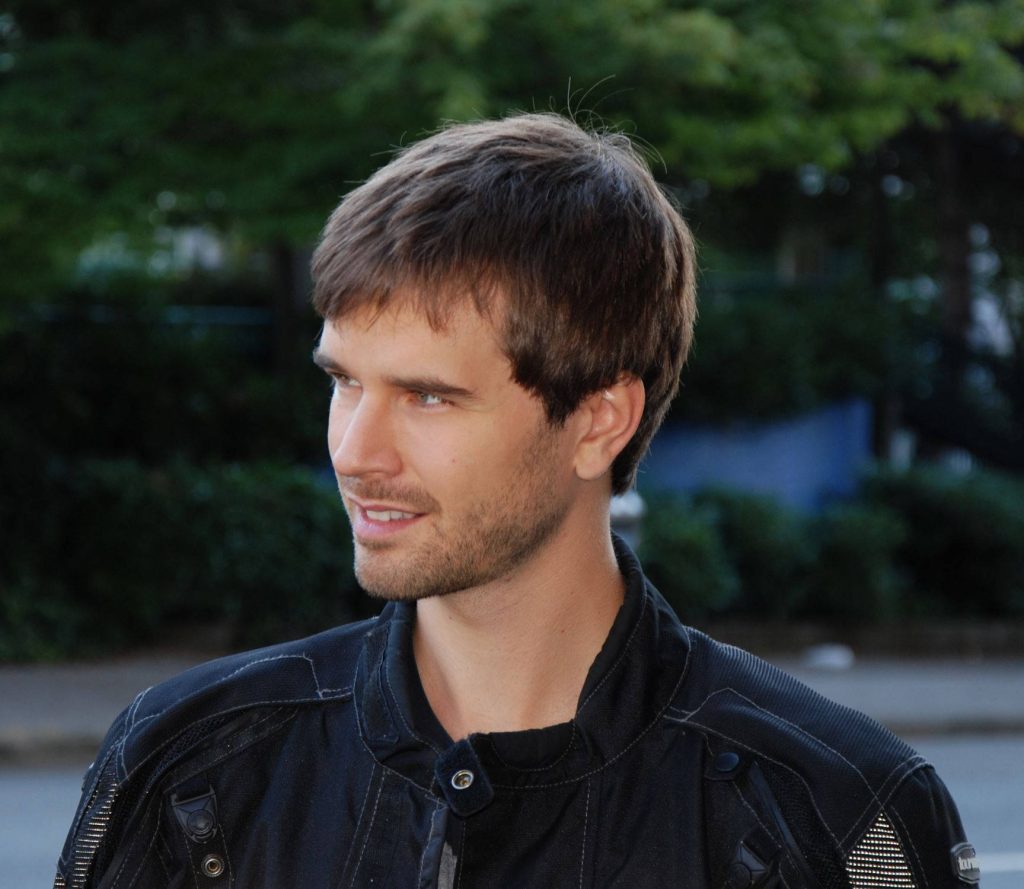 Graham Wardle portrait wallpaper in black motorcycle jacket with natural outdoor lighting and green blur background