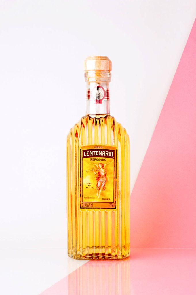 Gran Centenario Reposado Tequila ribbed glass bottle on white and pastel pink wallpaper background