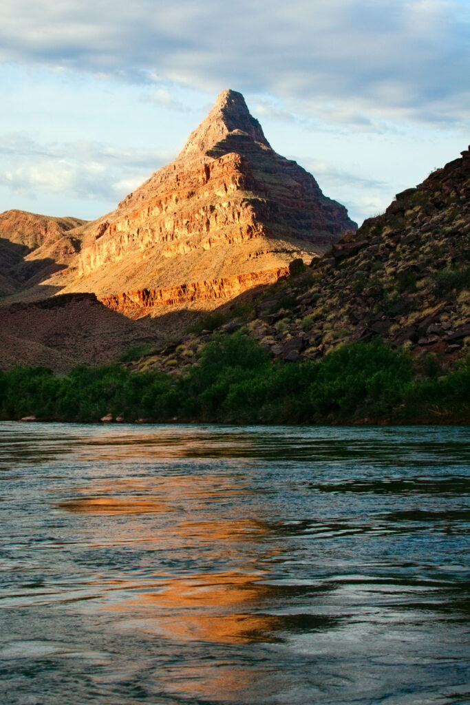 Grand Canyon landscape with rugged rocks warm sunlight serene lake and partly cloudy sky wallpaper