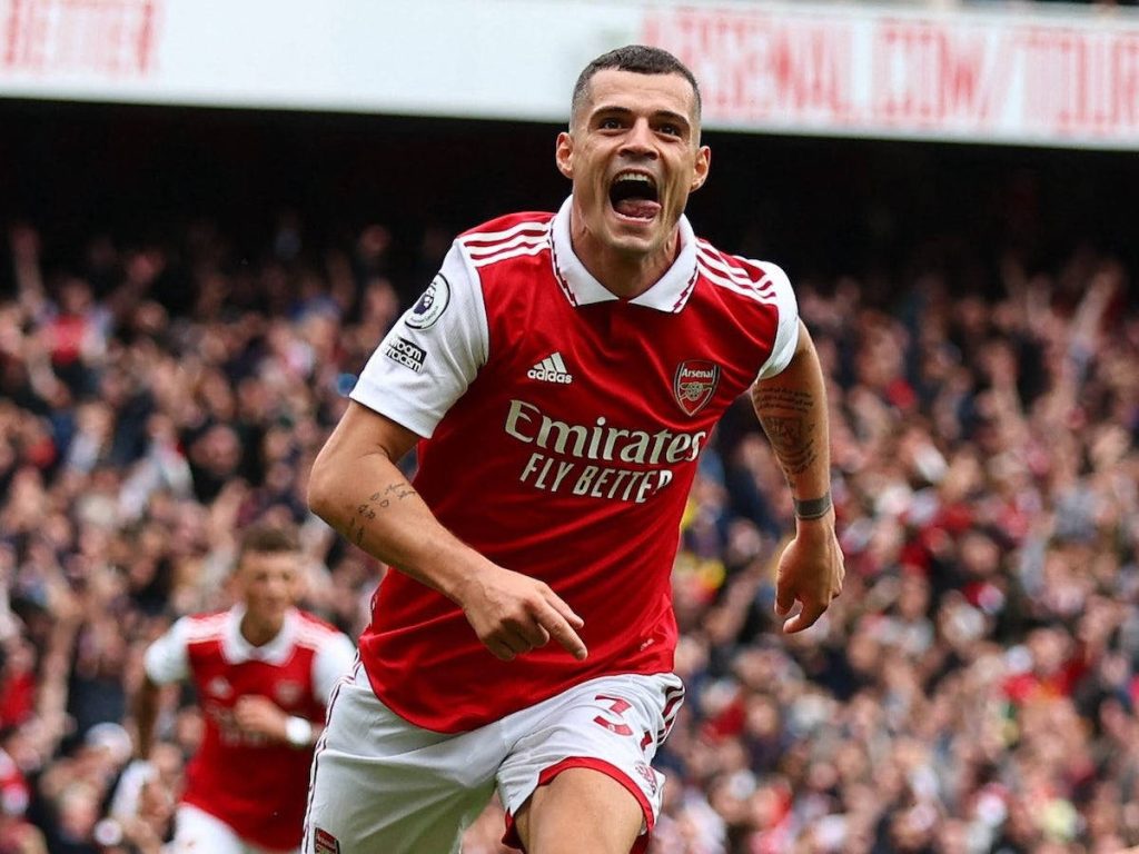Granit Xhaka celebrating in Arsenal red white Adidas kit blurred stadium crowd sports wallpaper
