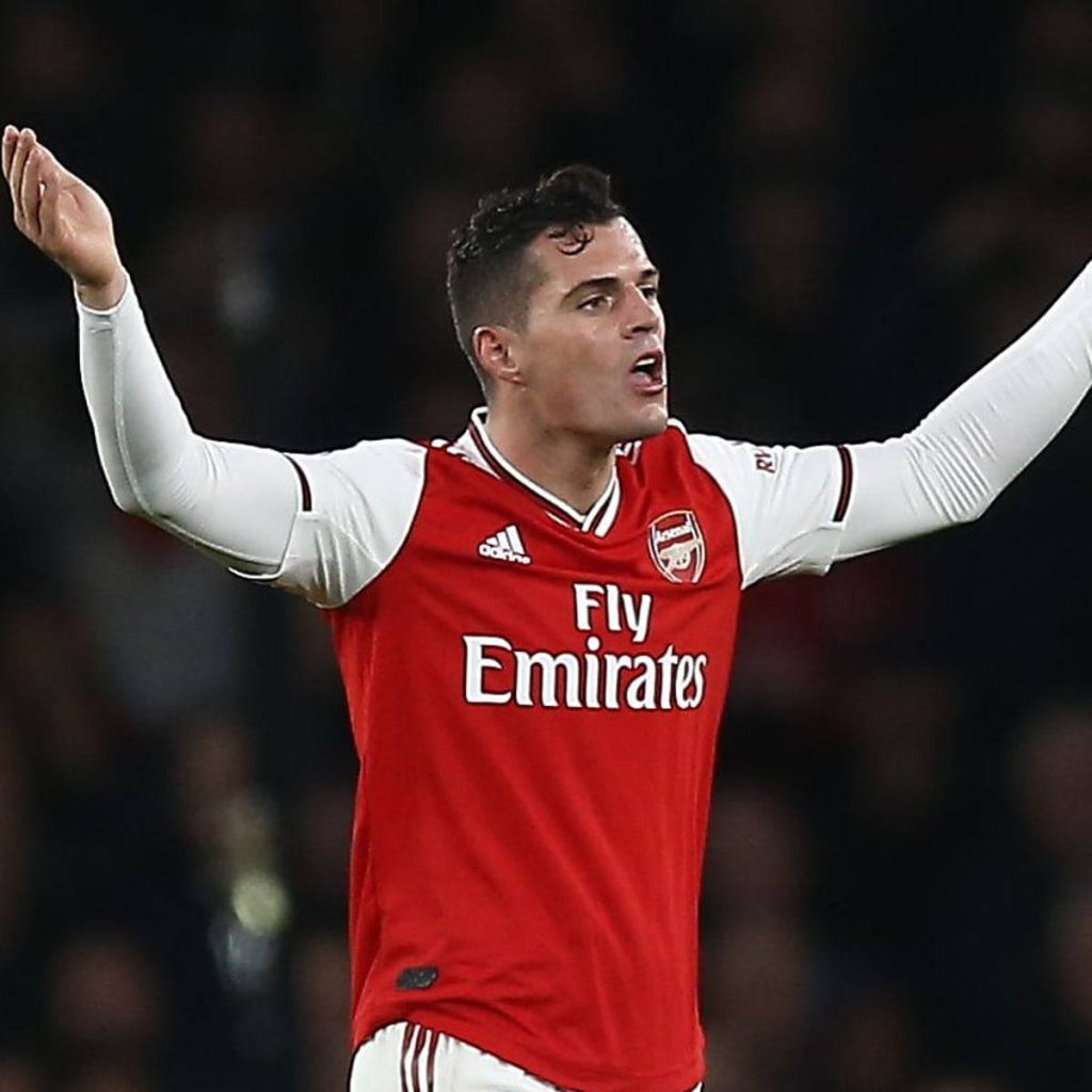 Arsenal midfielder Granit Xhaka in red home kit celebrating with raised arms stadium backdrop Wallpaper
