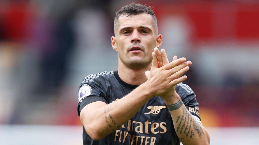 Granit Xhaka clapping in black Arsenal away kit with arm tattoos in stadium background wallpaper