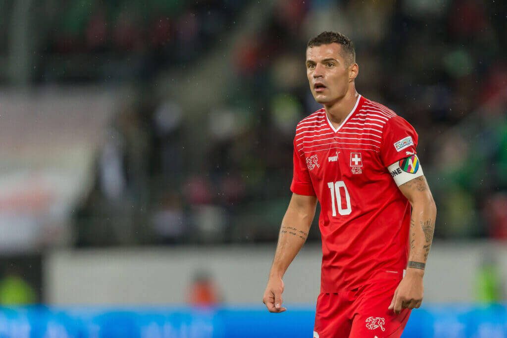 Granit Xhaka focused in red jersey number 10 football stadium background high-energy wallpaper