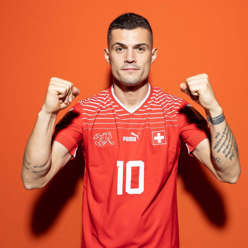 Swiss captain Granit Xhaka in red jersey clenches fists against bold orange background wallpaper