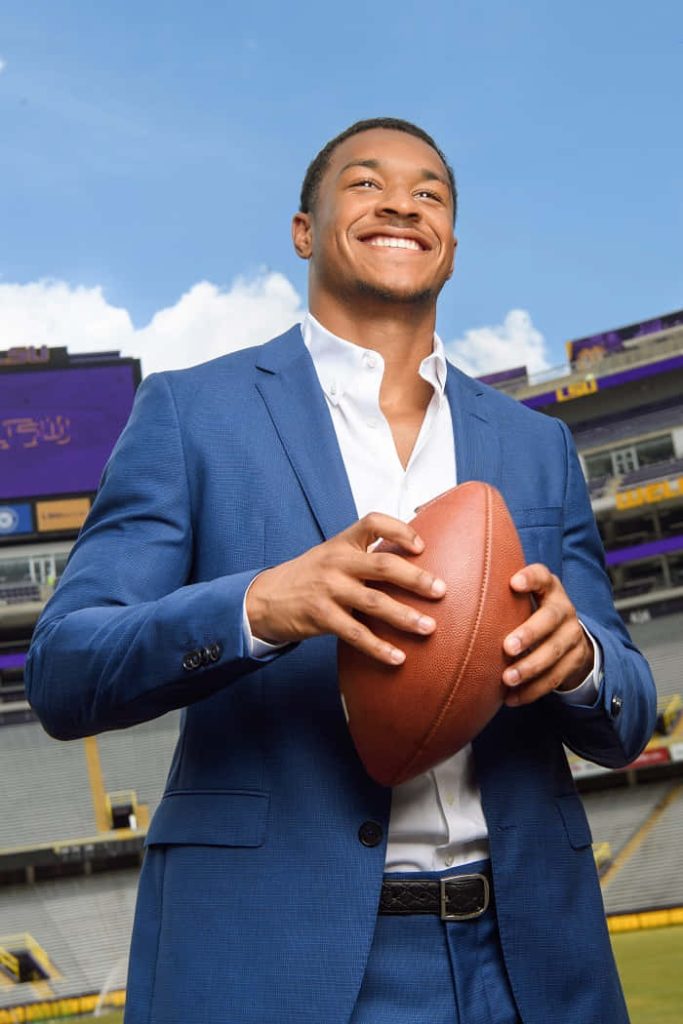 Professional portrait of NFL safety Grant Delpit in navy suit holding football at LSU Tiger Stadium Wallpaper
