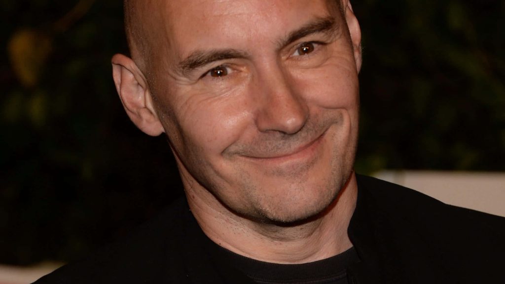 Close-up portrait of comic writer Grant Morrison with shaved head and gentle smile dark background Wallpaper