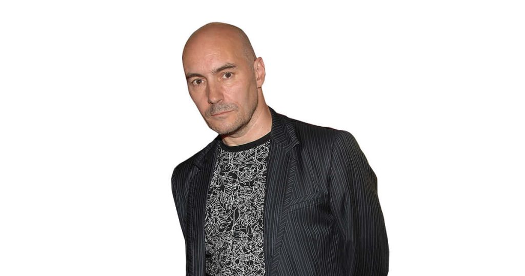Studio portrait of Grant Morrison in dark pinstripe blazer and graphic tee on white background Wallpaper