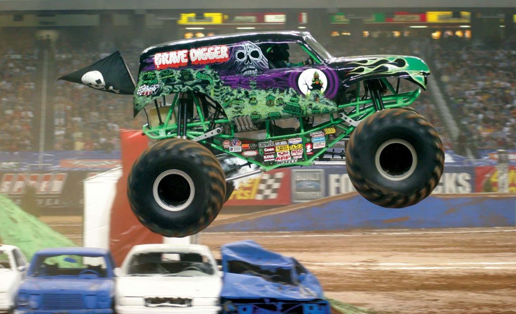 Grave Digger monster truck mid-jump over crushed cars on dirt track thrilling motorsport action Wallpaper