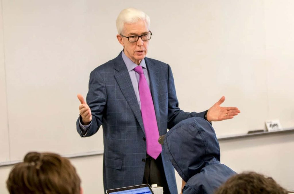 Former California Governor Gray Davis lecturing students in navy suit and purple tie classroom Wallpaper