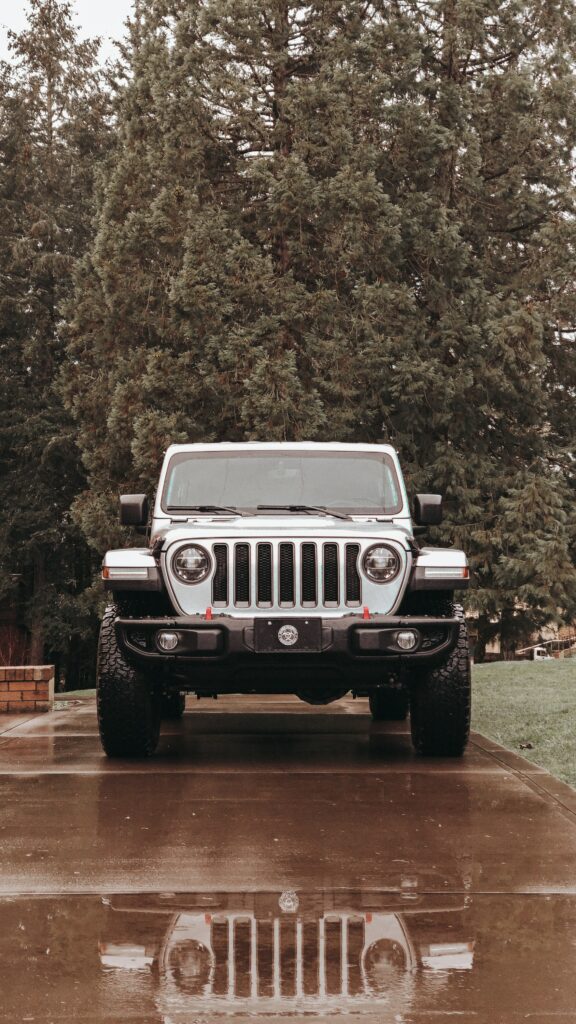 Gray Jeep Wrangler in Rainy Driveway Among Lush Trees Wallpaper