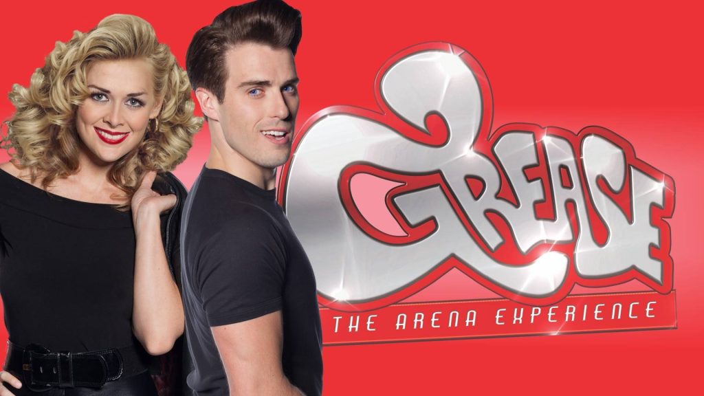 Grease The Arena Experience poster with actors as Sandy and Danny Zuko on red background Wallpaper