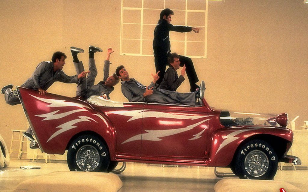 Grease wallpaper featuring John Travolta as Danny Zuko with red Greased Lightnin hot rod