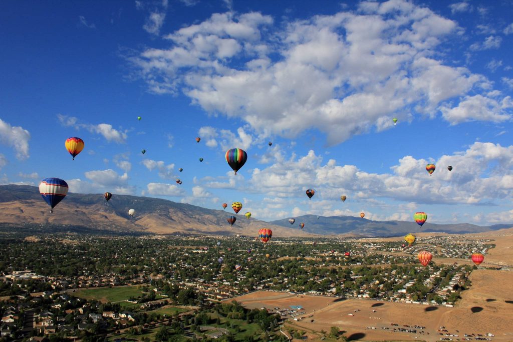 Colorful hot air balloons float over Reno Nevada desert mountains in bright blue sky wallpaper