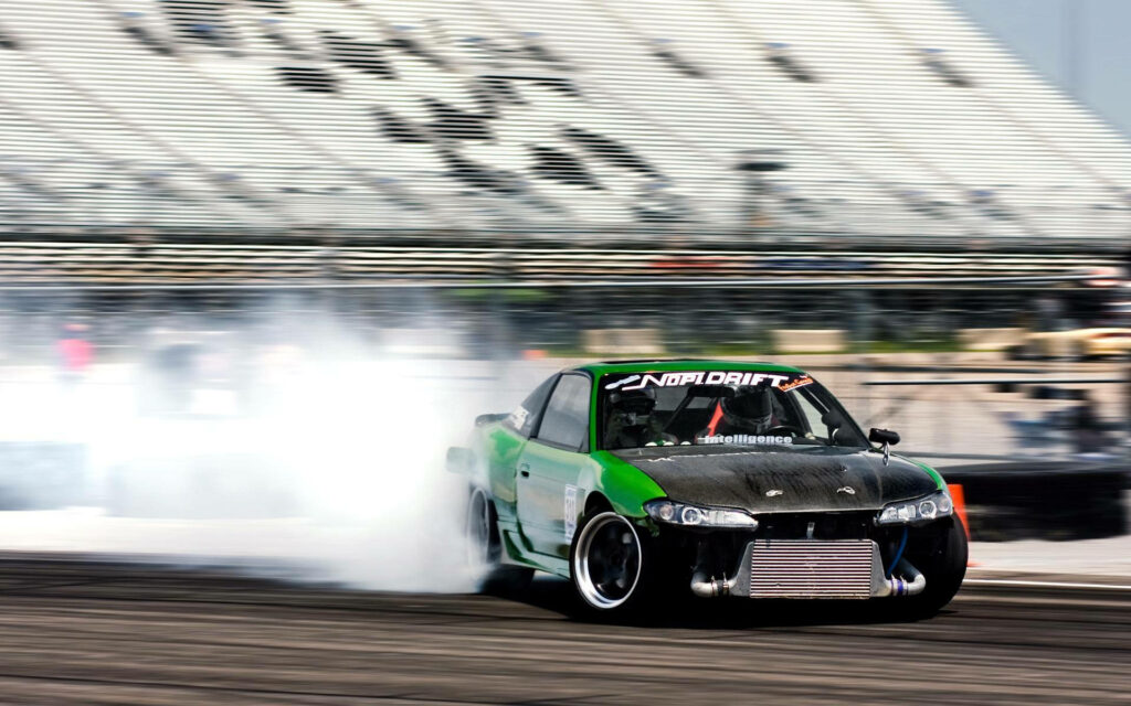 Green and black drift car kicking up smoke drifting sideways on racetrack with stadium seats Wallpaper