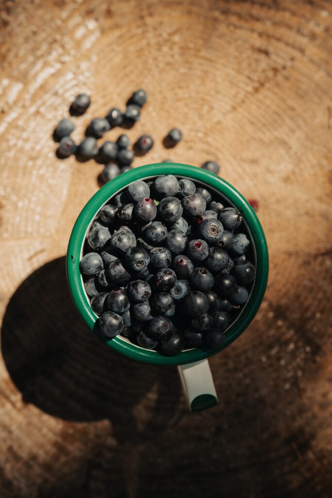 Fresh Blueberries in Green Cup on Wooden Surface Wallpaper Background