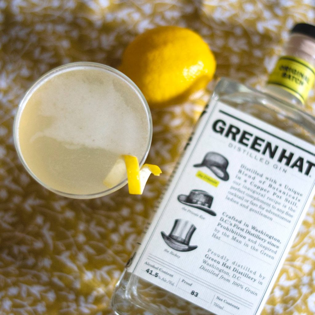 Green Hat Original Batch Gin bottle with lemon twist cocktail on textured yellow background Wallpaper
