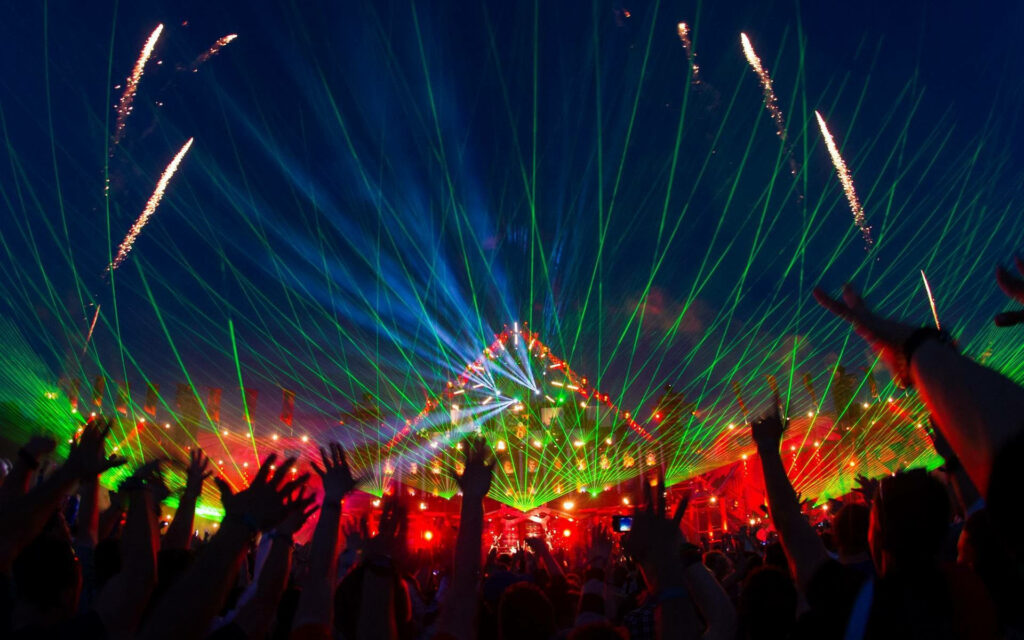 Cheering crowd at night concert with vibrant green laser lights bursting in dark sky background Wallpaper