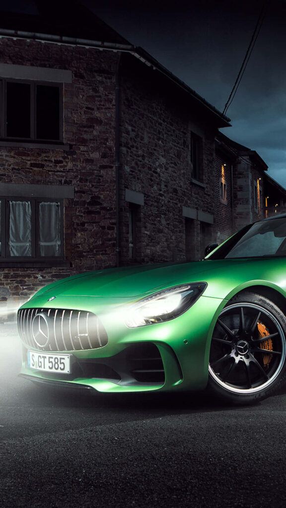 Green Mercedes AMG GT R parked on quiet night street with illuminated headlight and rustic buildings Wallpaper