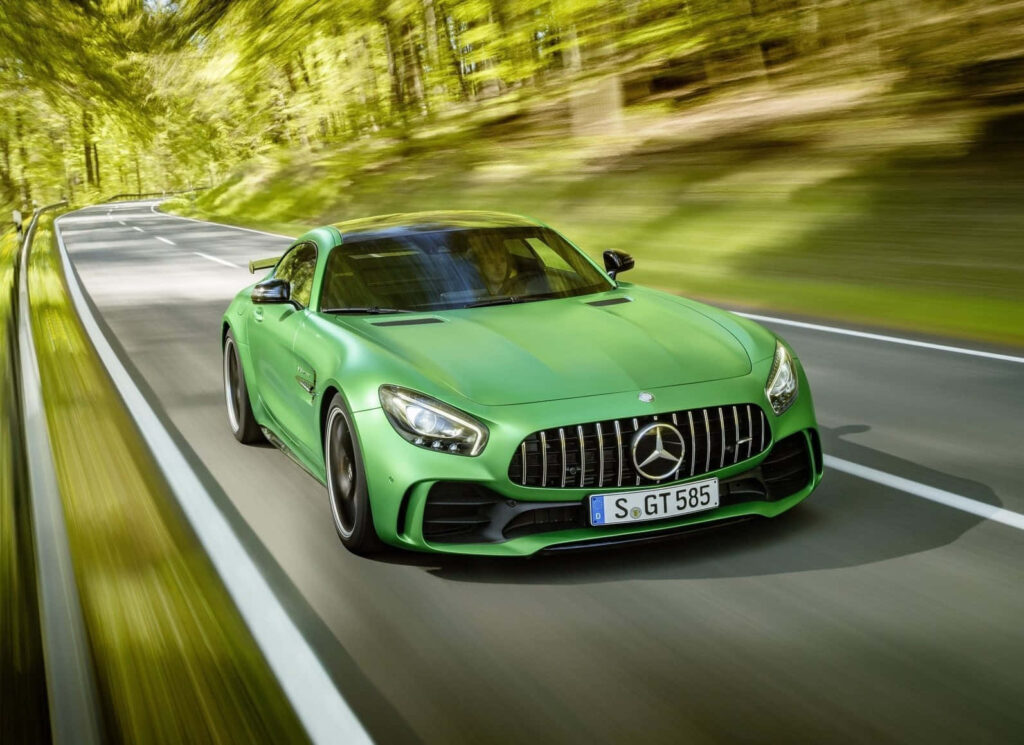 Green Mercedes AMG GT-R speeding on scenic forest road showcasing dynamic sports car design Wallpaper
