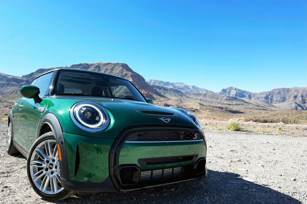 Green Mini Cooper in sunlit desert with rugged mountains and clear blue sky background wallpaper