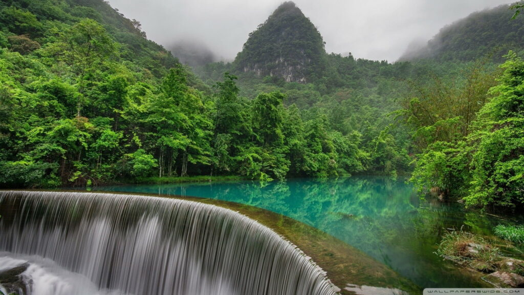 Crescent waterfall flowing into turquoise lake surrounded by misty lush mountain forests wallpaper